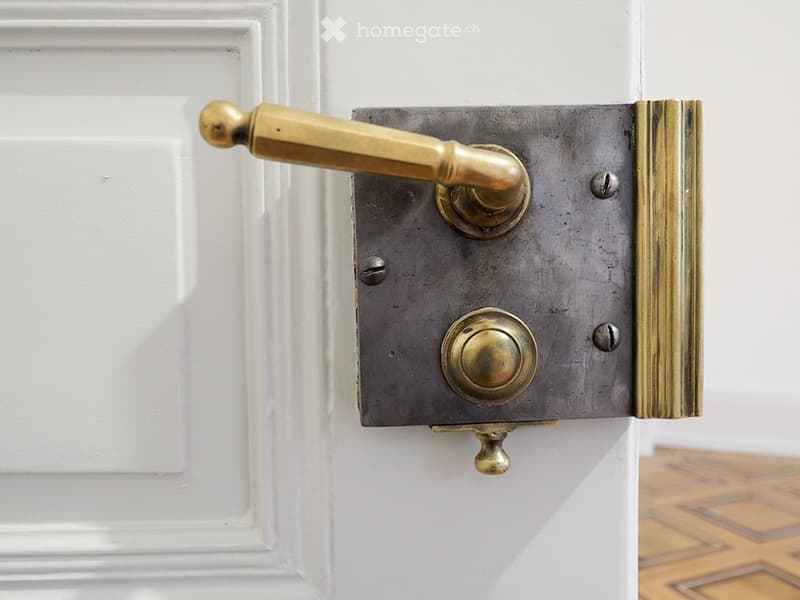 Close-up of a vintage brass door handle attached to a white door frame, with a polished brass lever and escutcheon plate.