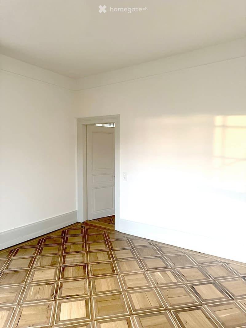 Empty room with white walls and a wooden floor, featuring a single door leading to another space.