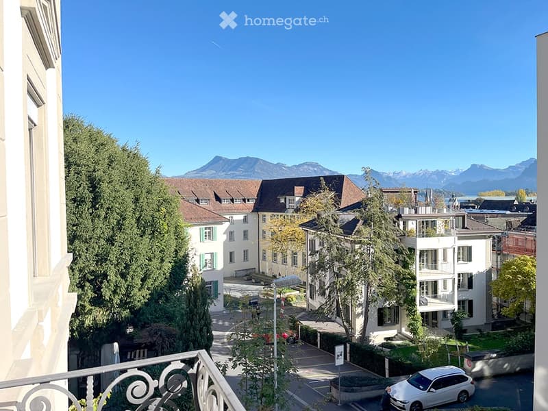 Balcony view overlooking a residential area with houses, trees, and distant mountains under a clear blue sky.