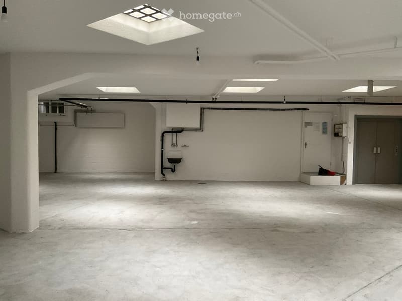 Empty garage with concrete floor, white walls, and minimal lighting. Features a sink, air conditioning unit, and a small storage area with a few items.