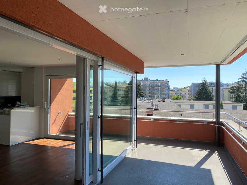 Modern balcony with glass sliding doors, wooden flooring inside, and a view of the cityscape and rooftops.