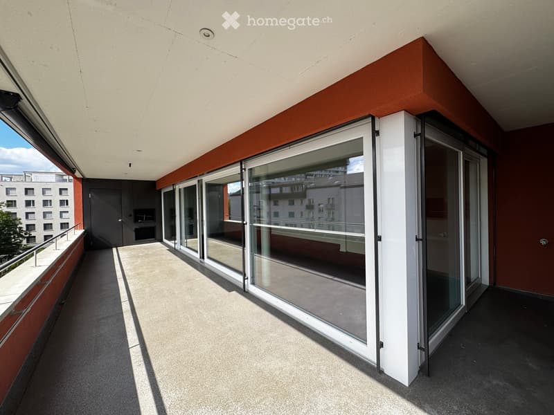 Modern balcony with large glass sliding doors, white railings, and a view of surrounding buildings.