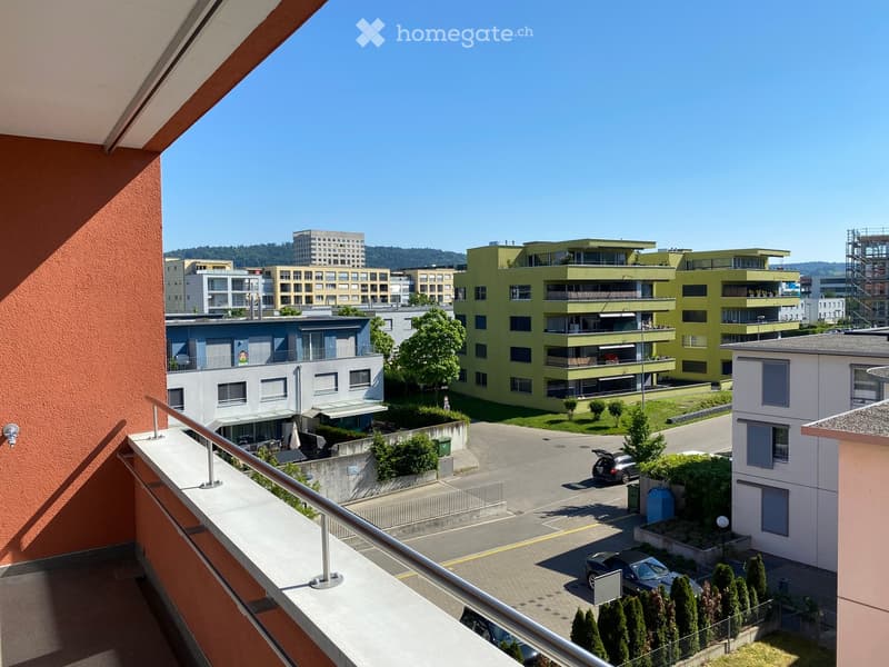 Balcony overlooking a modern residential complex with multiple buildings, parking area, and greenery.