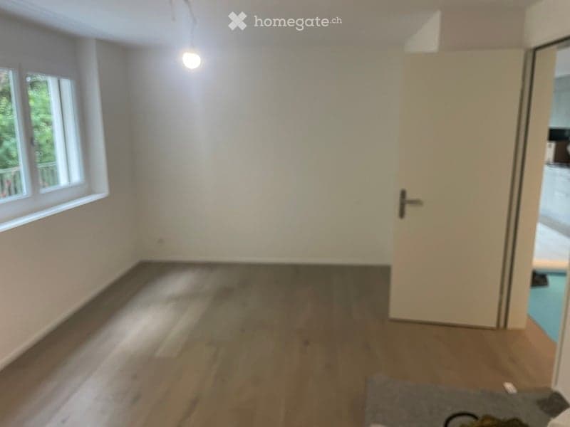 Empty room with wooden flooring, white walls, and large windows allowing natural light. No furniture or equipment present.