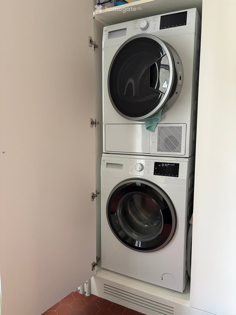 A compact bathroom with a stacked washing machine and dryer unit, featuring a control panel and a small shelf above.