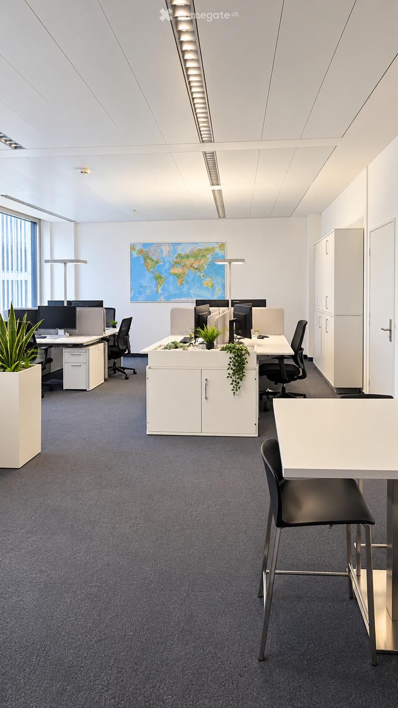 Modern office space with desks, chairs, computer monitors, cabinets, and a world map on the wall.