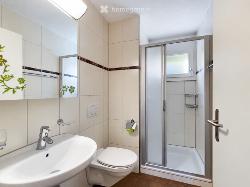 Modern bathroom with a white sink, chrome faucet, toilet, glass-enclosed shower, and a large mirror with decorative floral stickers.