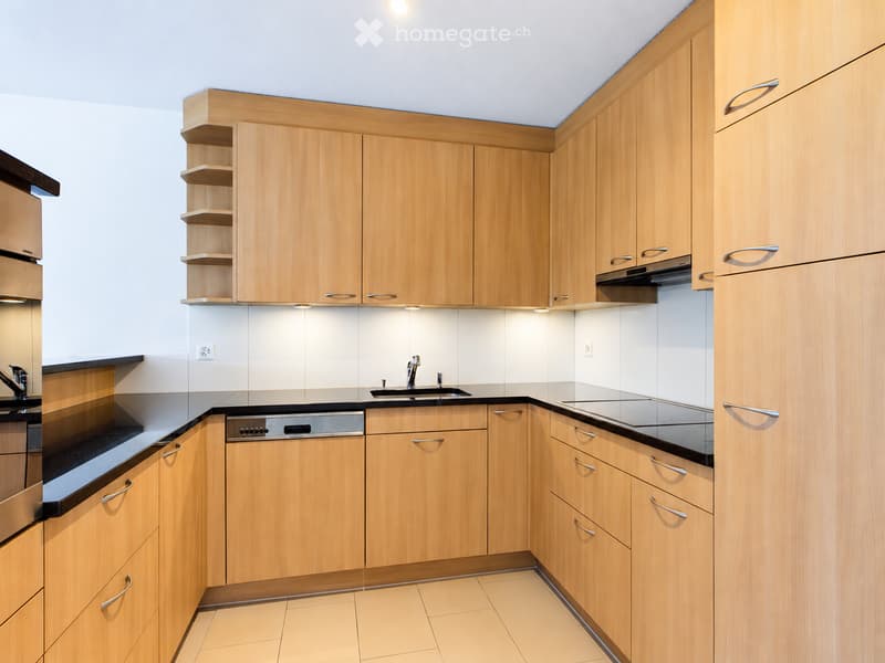 Modern kitchen with light wooden cabinets, black countertops, a sink, a dishwasher, and an oven.