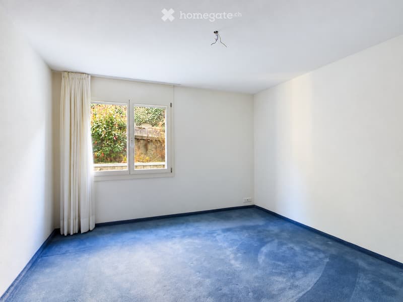 Empty room with light-colored walls, blue carpet, and a window with white curtains. No furniture or equipment is present.