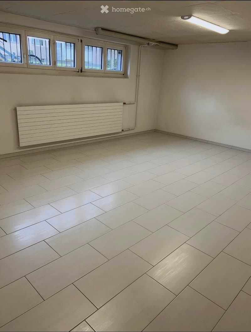 Empty room with tiled floor, white walls, radiator, and windows with metal bars.
