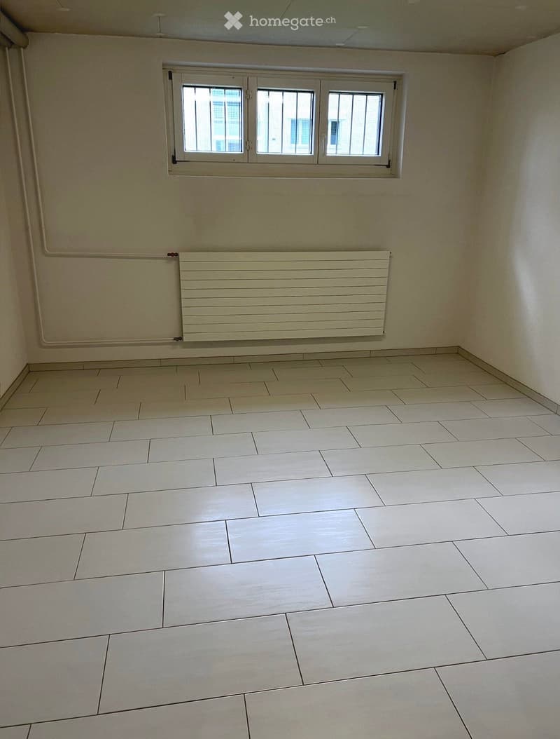 Empty room with beige tiled floor, white walls, and a window with three panes. A radiator is mounted on the wall below the window.