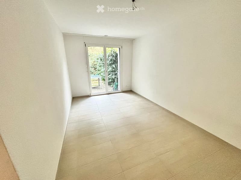 Empty room with tiled floor and white walls, featuring a sliding glass door leading to an outdoor area.