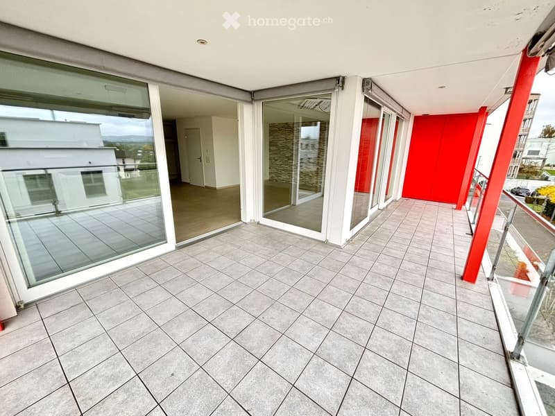 Balcony with tiled floor, large glass sliding doors, red accent wall, and a view of the surrounding area.