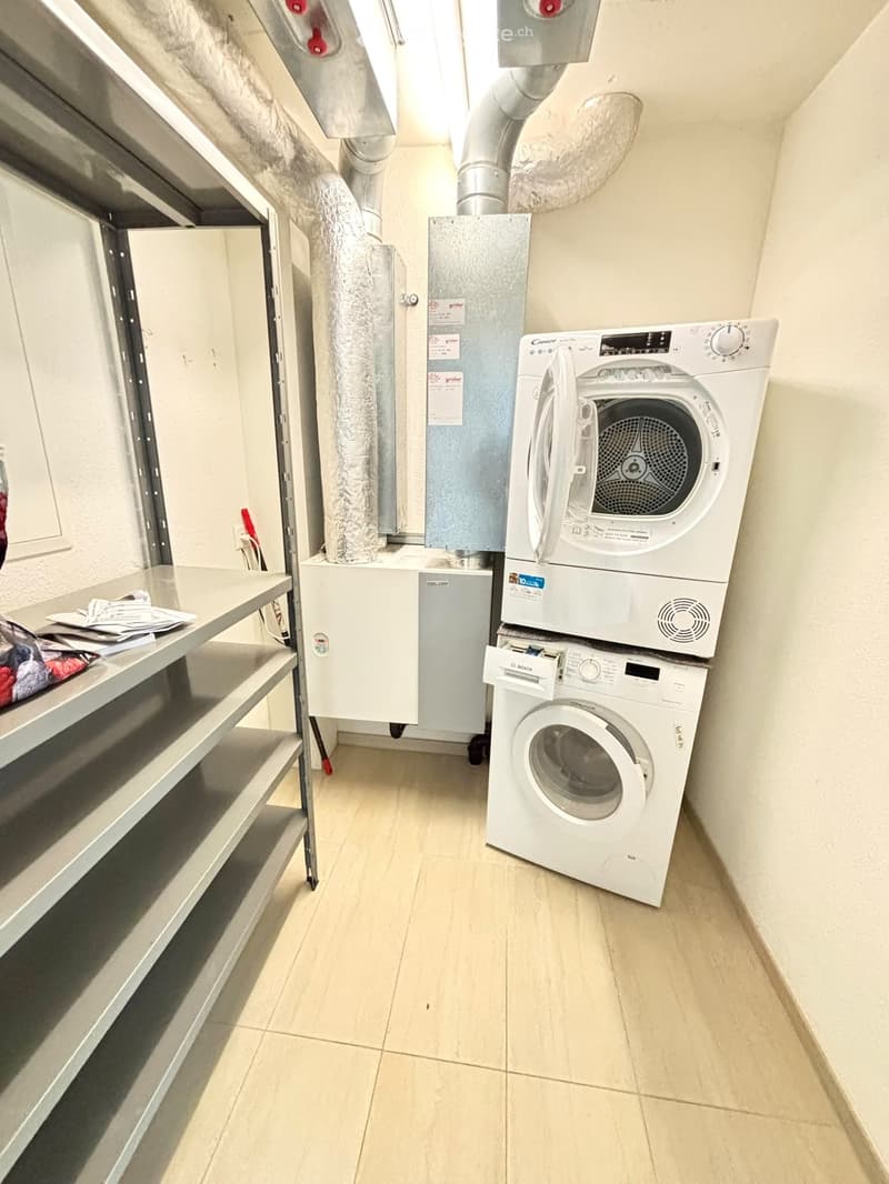 A small utility room with a washing machine and a dishwasher, metal shelving unit, and a tiled floor.
