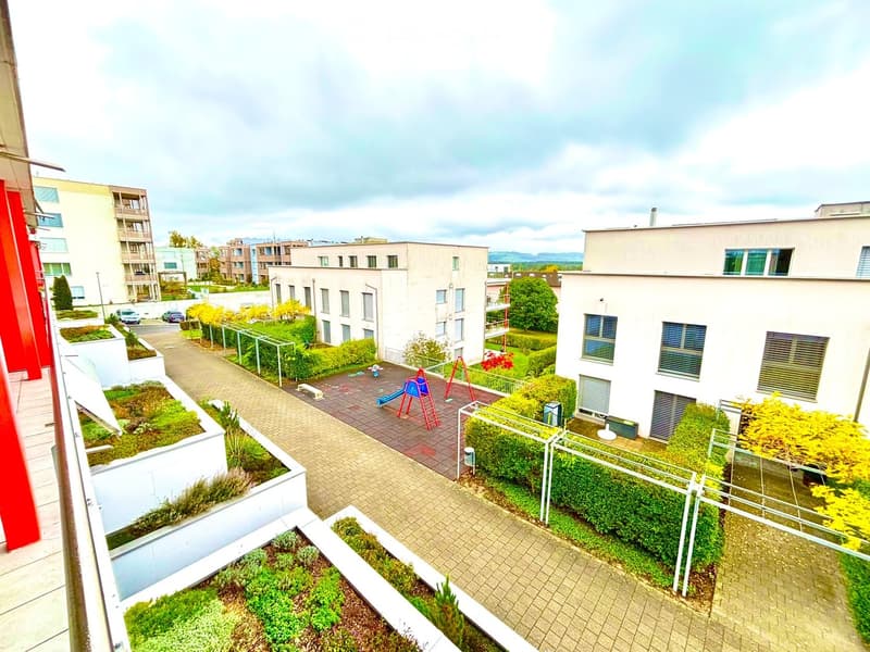 View from a balcony showing a landscaped garden area with pathways, greenery, and a small playground with slides and climbing equipment.