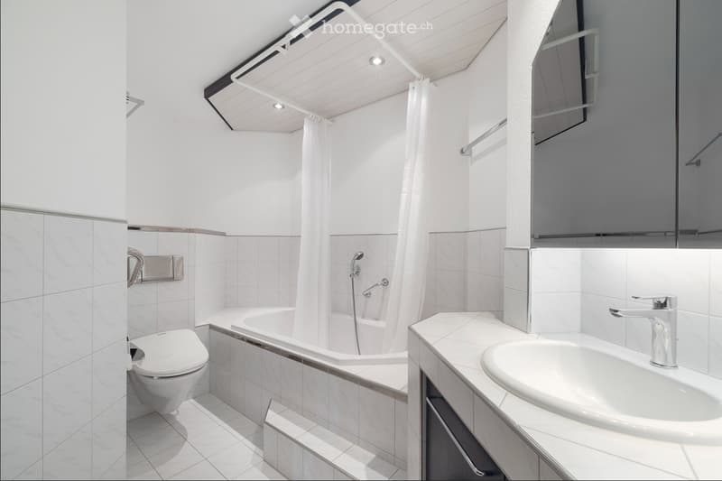 Modern bathroom with white tiles, bathtub, shower curtain, toilet, sink, and mirror.