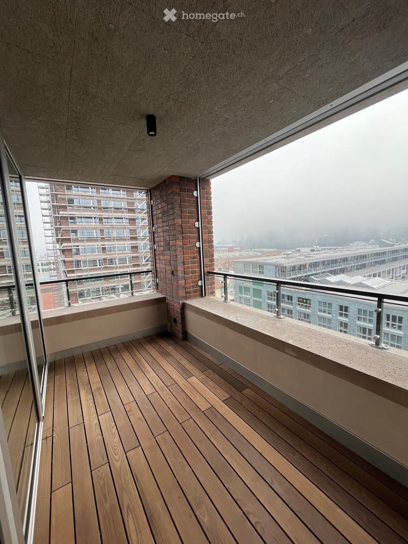 Wooden deck balcony with modern railing, overlooking cityscape with buildings and foggy skyline.