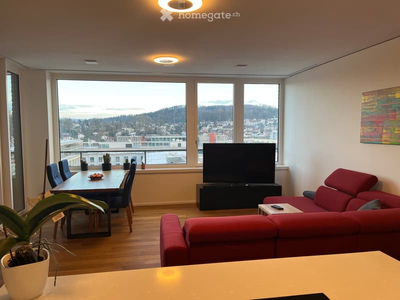 Modern living room with a red sofa, wooden dining table, chairs, TV, and a scenic city view through large windows.