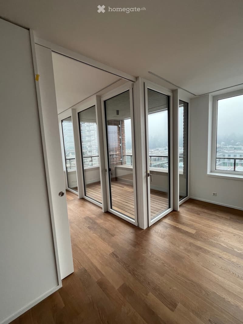 Empty room with wooden flooring, large glass sliding doors leading to a balcony, and white walls.