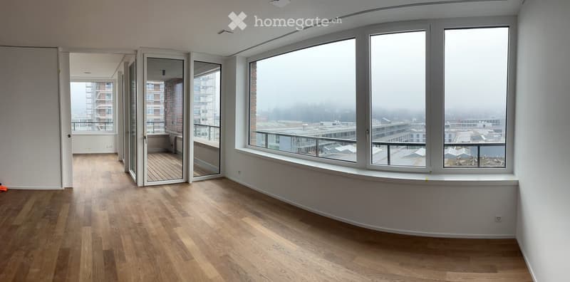Empty room with wooden flooring, large windows, and a sliding glass door leading to a balcony.