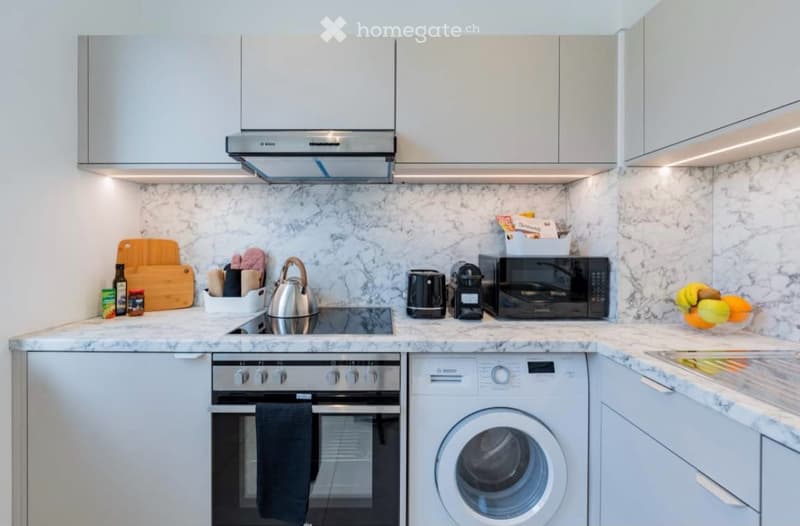 Modern kitchen with white cabinets, marble countertops, stainless steel appliances, and various kitchen tools and items neatly arranged.