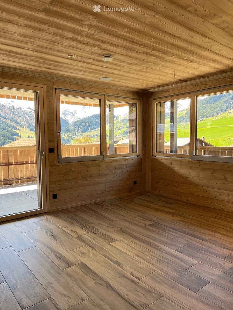 Empty room with wooden walls, ceiling, and flooring, large windows offering a scenic mountain view.
