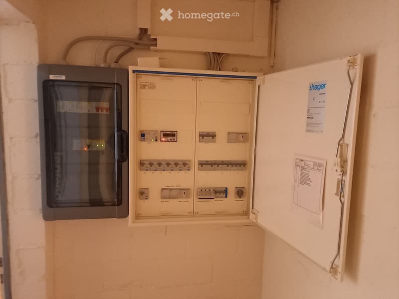 An electrical panel and circuit breaker box mounted on a wall, with visible wiring and labels.