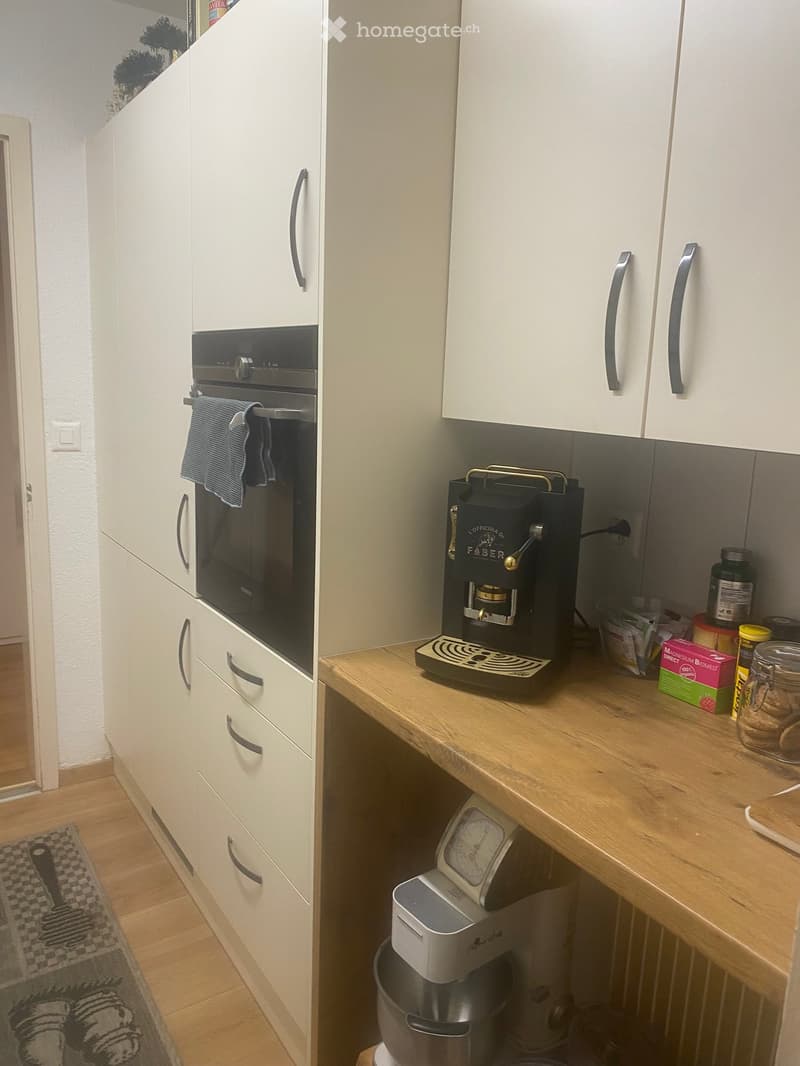 Modern kitchen with white cabinets, wooden counter, coffee maker, oven, and various small items on the counter.