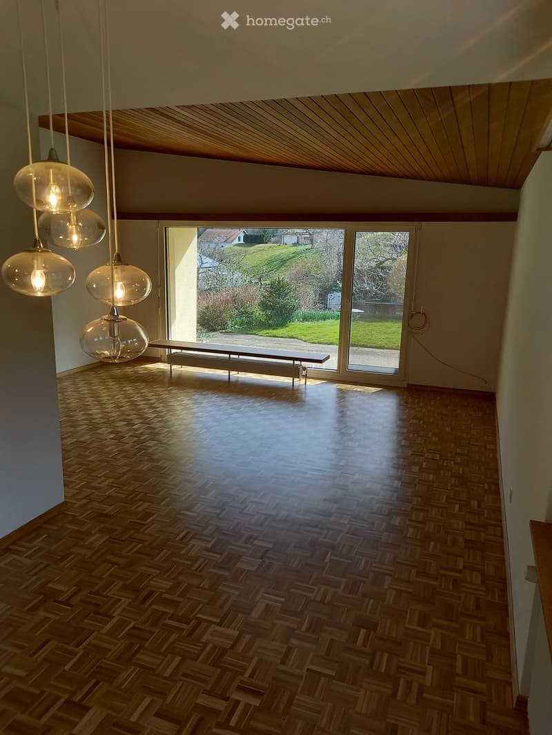 Empty room with wooden herringbone flooring, large windows, and modern pendant lights. No furniture or equipment present.