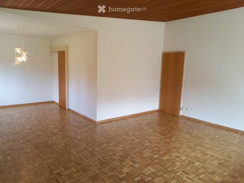 Empty room with wooden parquet flooring, white walls, and a wooden ceiling. Two wooden doors are visible, one on each side of the room.