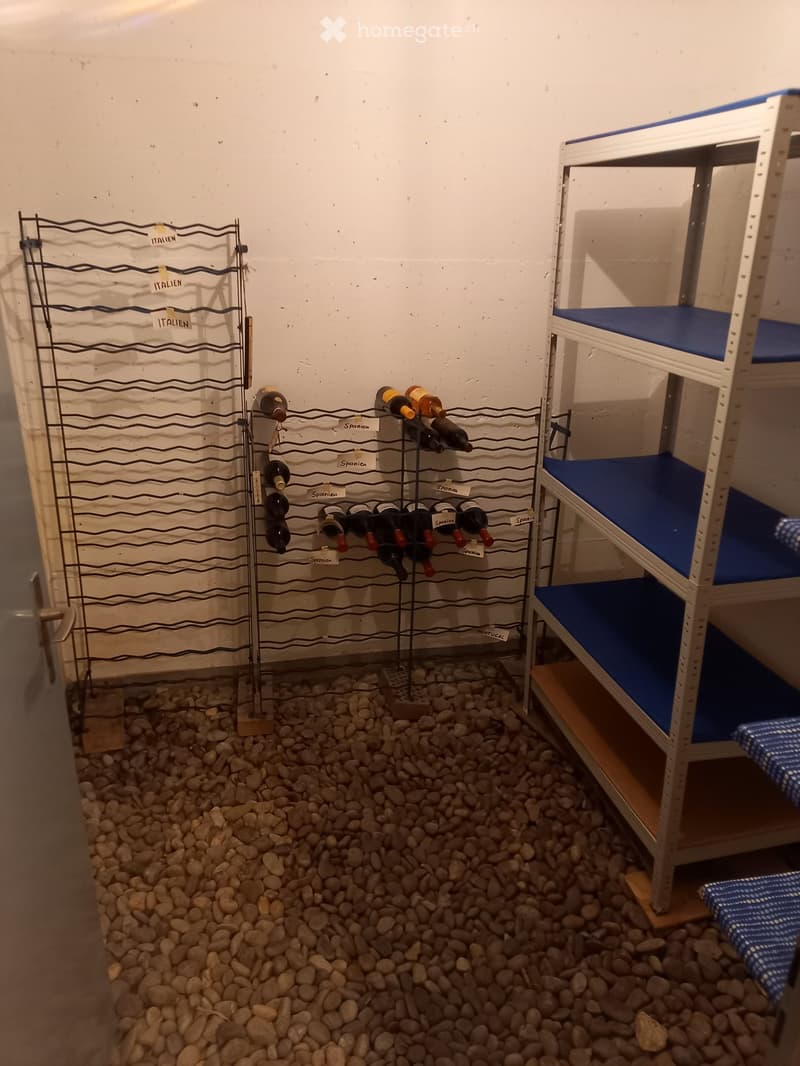 A small room with a wine rack holding several bottles and a bunk bed with blue mattresses.