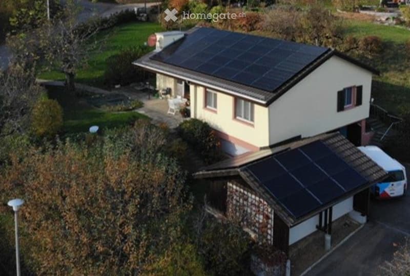 A two-story house with solar panels on the roof, a garage, and a parking area.