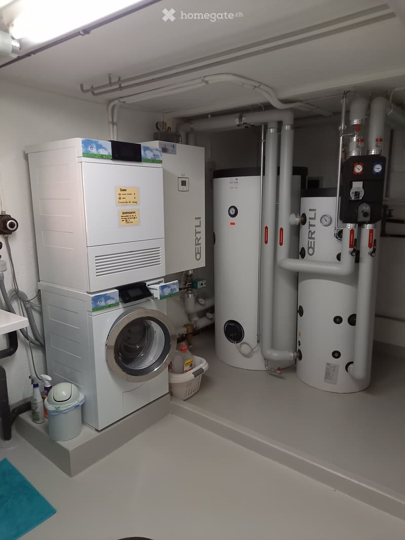 Utility room with a washing machine, water heater, control panel, and a small trash bin.