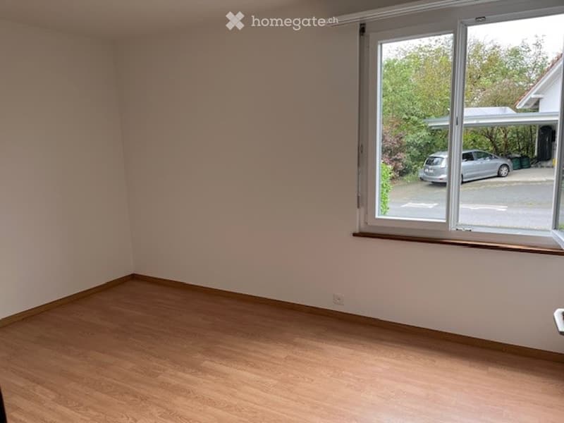 Empty room with wooden flooring and large window showing a parked car outside.