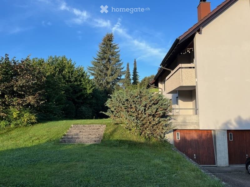 A modern two-story house with a balcony, garage, and well-maintained garden area with steps leading up to the entrance.