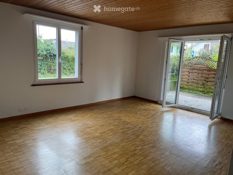 Empty room with wooden flooring, large window, and open sliding doors leading to an outdoor area.