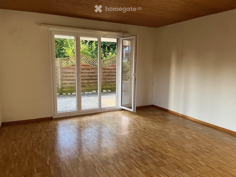 Empty room with wooden flooring, white walls, and large sliding glass doors leading to an outdoor area.