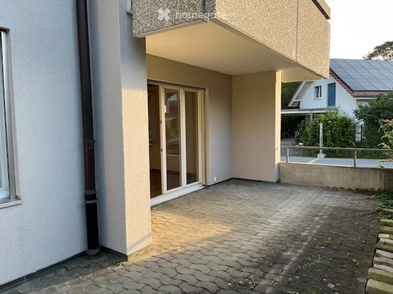 Balcony area with a paved brick floor, large glass sliding doors leading to the interior, and a small raised platform with a railing.