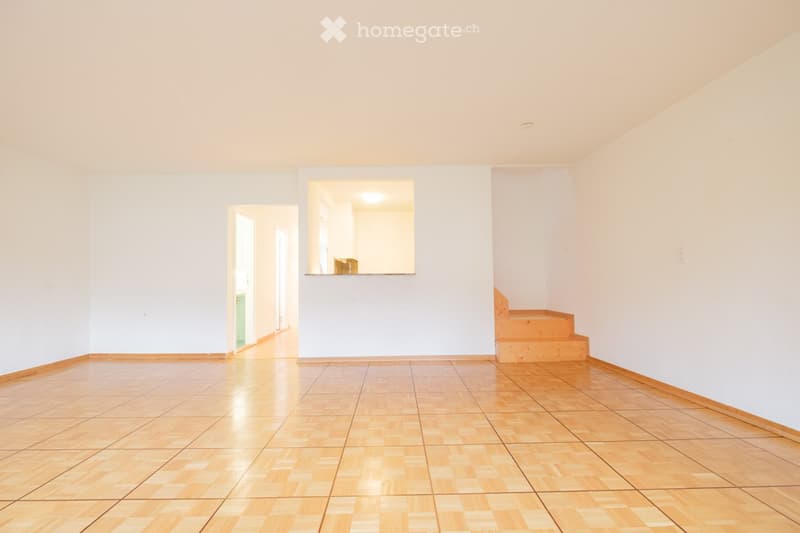 Empty room with wooden flooring, white walls, and a staircase leading upwards. No furniture or personal items are present.