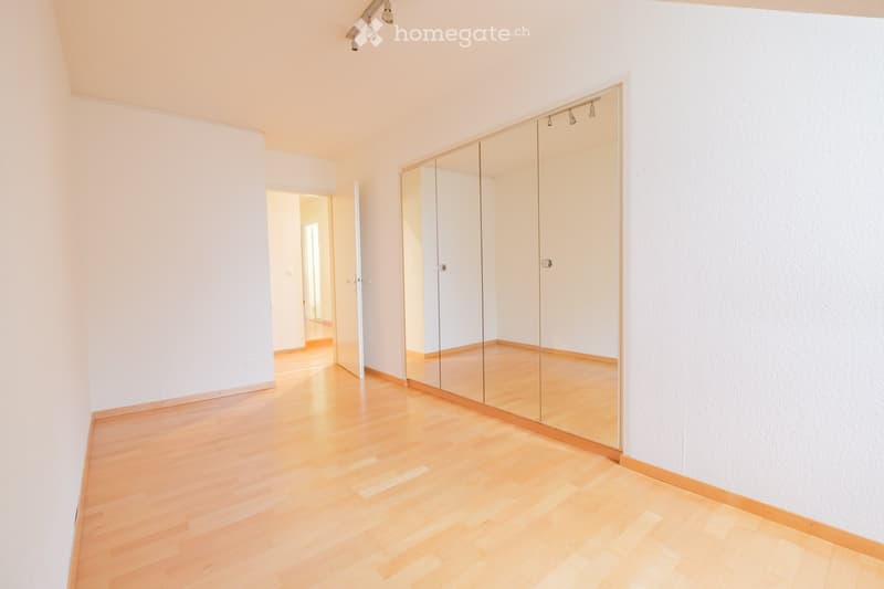 Empty room with light wooden flooring, white walls, and a large mirrored wardrobe. No furniture or equipment present.