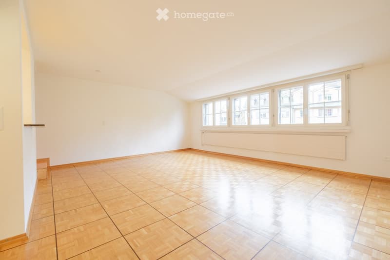 Empty room with wooden flooring, white walls, large windows, and a radiator. No furniture or equipment present.