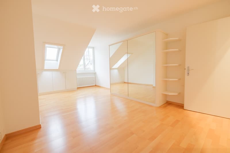 Empty room with wooden flooring, white walls, large mirror, built-in shelves, and windows with blinds.