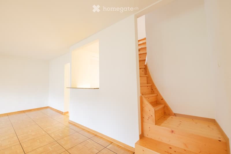 Empty hallway with wooden flooring, white walls, and a wooden staircase leading upwards.