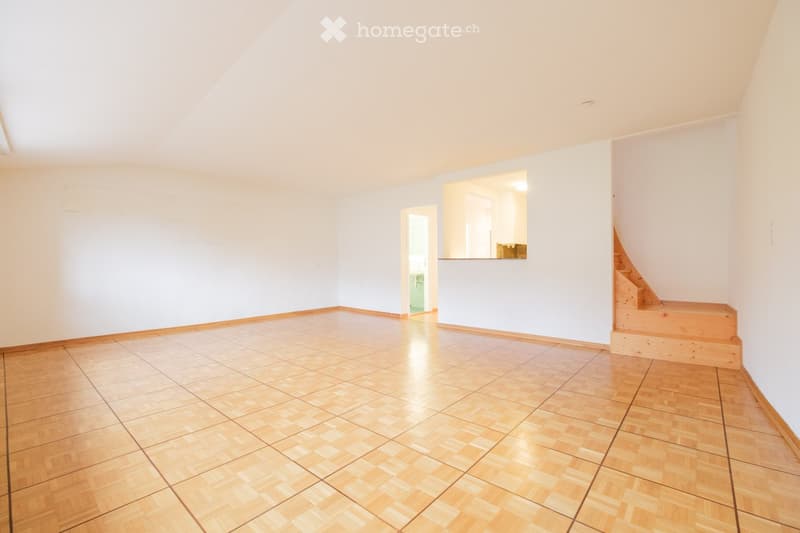 Empty room with wooden flooring and white walls, featuring a staircase leading to another level and an open doorway to an adjacent space.