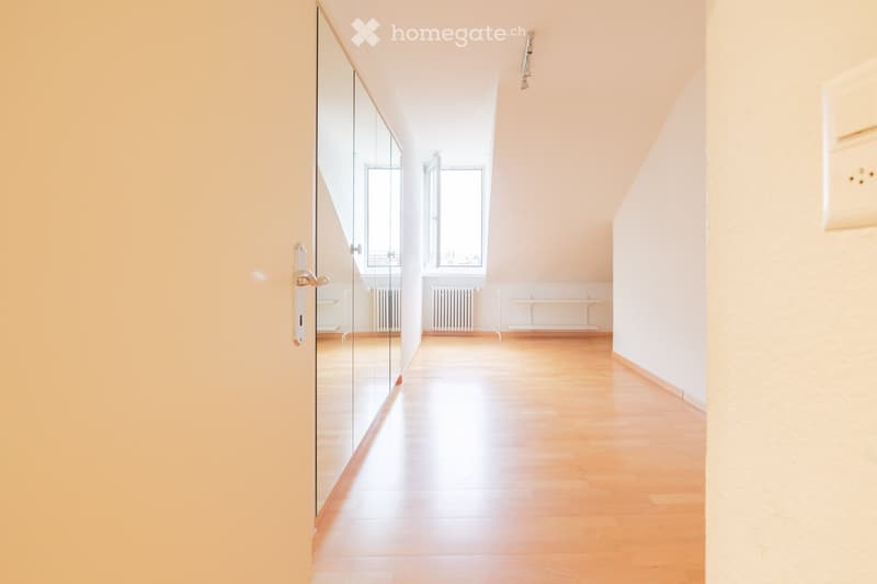 Empty hallway with wooden flooring, white walls, and large windows at the end. A glass door is visible on the left side.