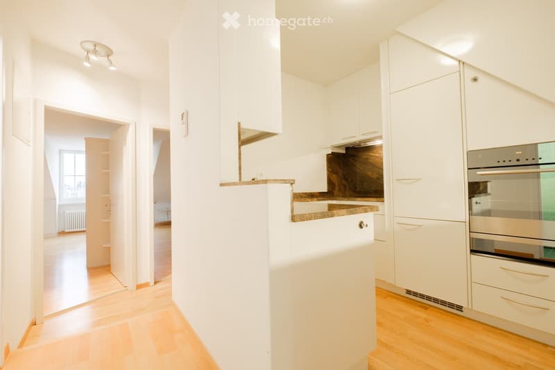 Modern kitchen with white cabinets, a stainless steel oven, and a wooden countertop. The space features light wooden flooring and recessed lighting.