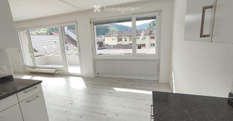 Bright, unfurnished room with large windows, white walls, and light wooden flooring. Minimalist design with no furniture.
