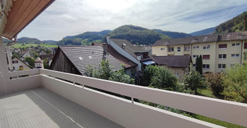 Balcony with a scenic view of a town and surrounding mountains, featuring a white railing and tiled floor.