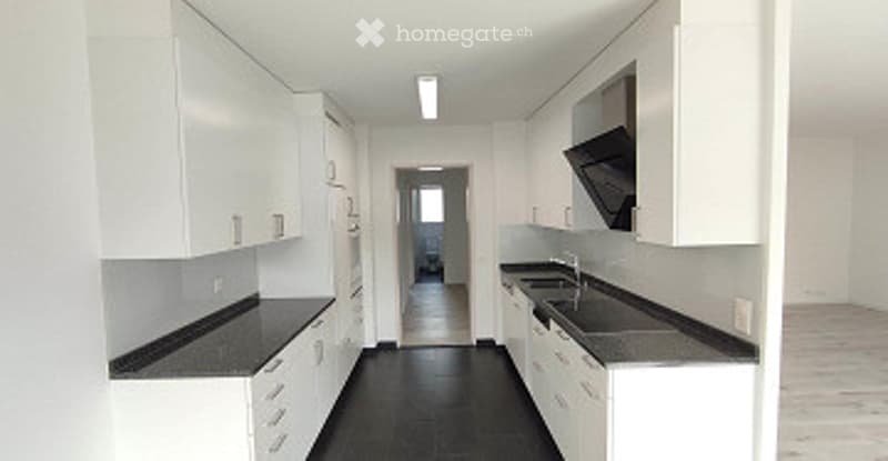 Modern, minimalist kitchen with white cabinets, black countertops, and a black floor. The space is completely empty, with no appliances or furniture.
