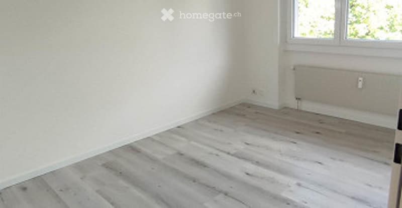 Empty room with light wooden flooring, white walls, and a single window with natural light. No furniture or equipment present.